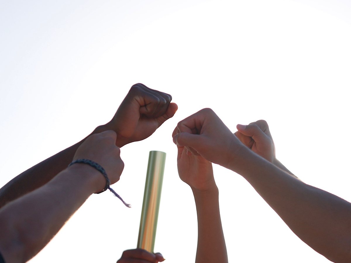Athletes putting hands in around a relay baton